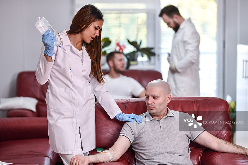 护士在化疗期间安抚疲惫的癌症患者，而另一位护士正在后面准备图片素材