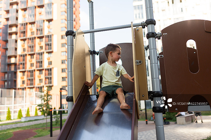 夏天，小男孩坐在游乐场滑梯顶端图片素材