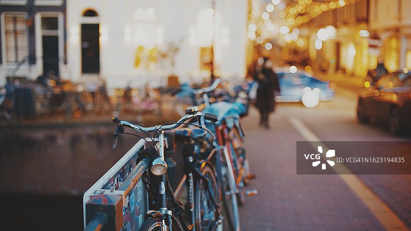 黄昏时分停靠在阿姆斯特丹灯火通明城市栏杆旁的自行车图片素材