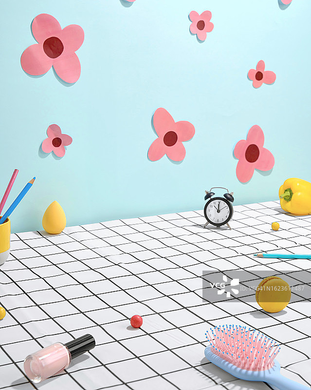 摆放着办公用品的桌子：鲜花、指甲油、发刷、蜡笔、马卡龙、闹钟和甜椒点缀的蓝色背景，完美的女性工作场所抽象摄影图片素材