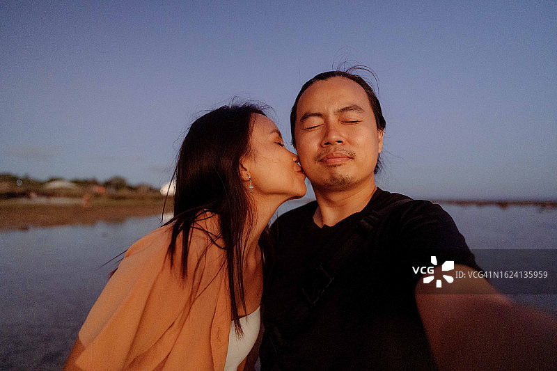 在海滩日落时自拍的亚洲情侣图片素材