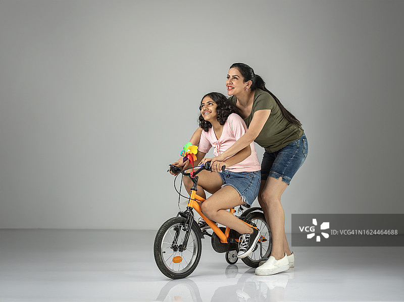 母亲帮助女儿在白色背景上骑自行车图片素材