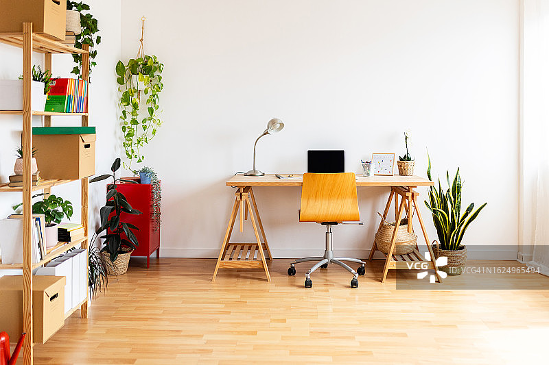 明亮房间内，木桌上放置笔记本电脑的现代家庭工作区内景图片素材