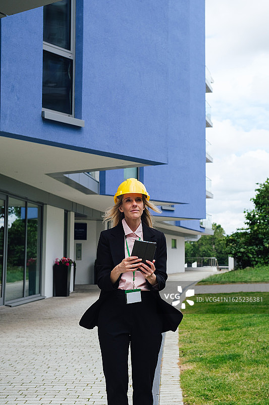 戴着安全帽在户外使用平板电脑的金发女建筑师图片素材