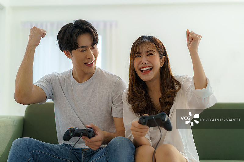 亚洲夫妇在家里的沙发上玩游戏图片素材