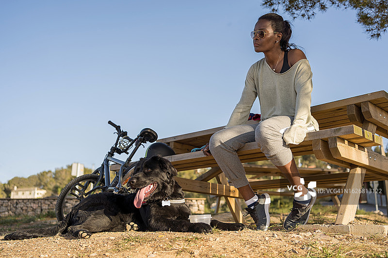 女人坐在木制长椅上，旁边有一只黑狗图片素材