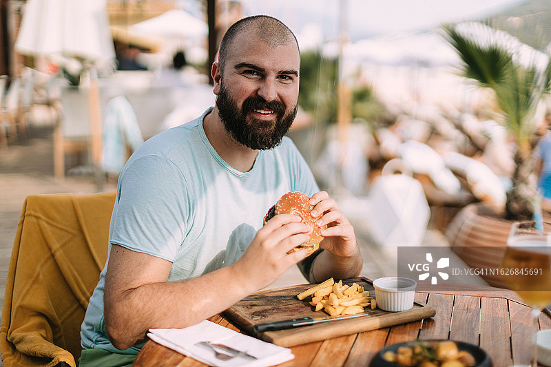 在海滩酒吧度假时吃汉堡和薯条的年轻男人图片素材