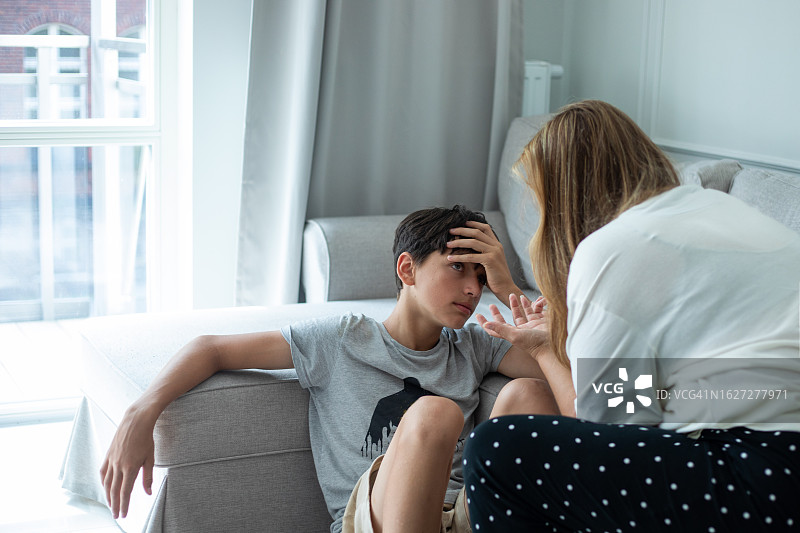 母亲坐在沙发上，靠近十几岁的儿子，与看着父母的男孩交谈图片素材