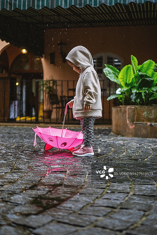 雨中撑着粉色雨伞的连帽衫小女孩图片素材