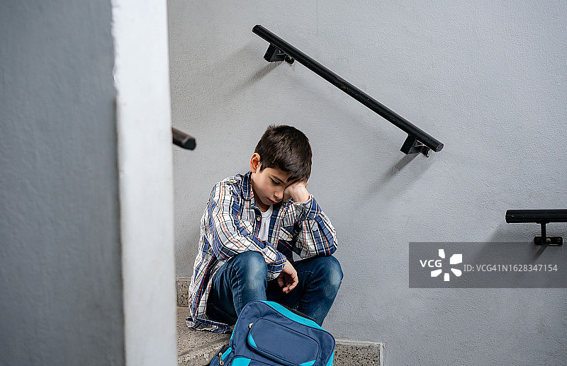 悲伤的小男孩坐在学校的楼梯上，看起来沮丧而孤独图片素材