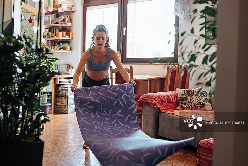 孕妇在公寓里铺开瑜伽垫，准备做瑜伽图片素材