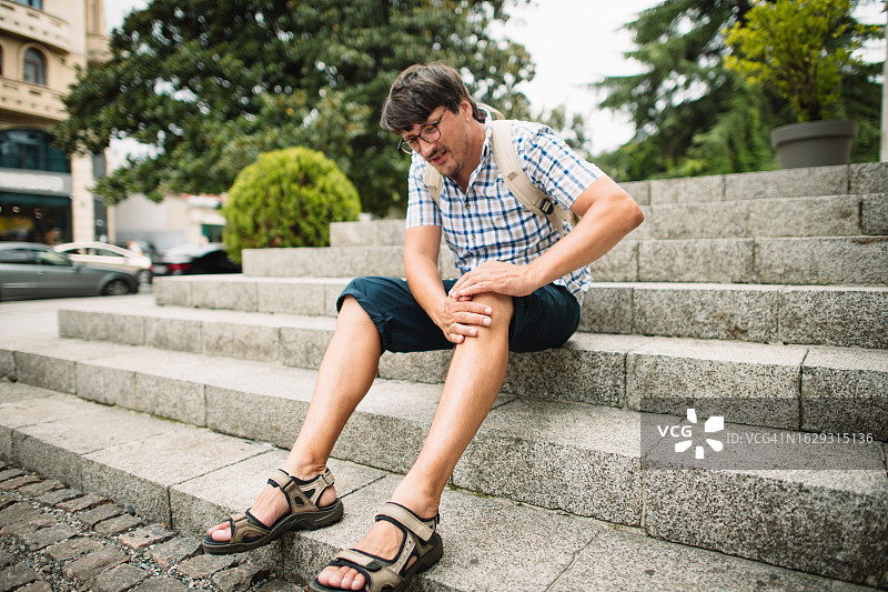 在夏日城市街道上膝盖疼痛的男人图片素材