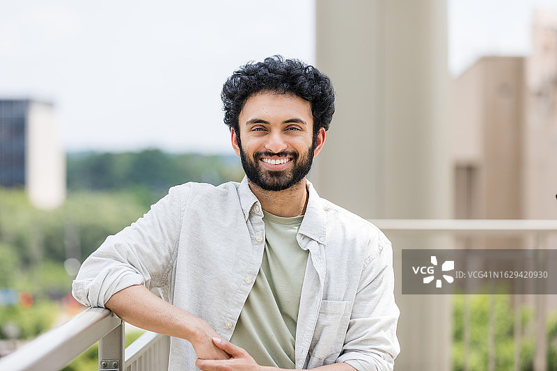倚靠在公寓阳台栏杆上的年轻男子图片素材