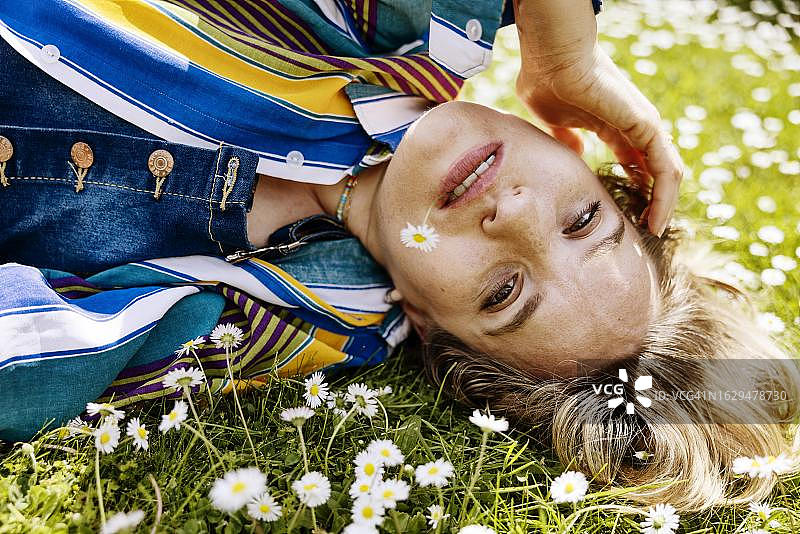 嘴里含着雏菊，躺在德国北莱茵-威斯特法伦科隆雏菊花丛草地上的年轻漂亮女人图片素材