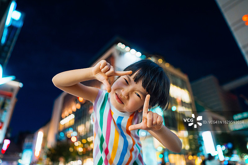 可爱亚洲小女孩在彩色灯光城市街道上手作取景框特写广角人像，旅行探索概念图片素材