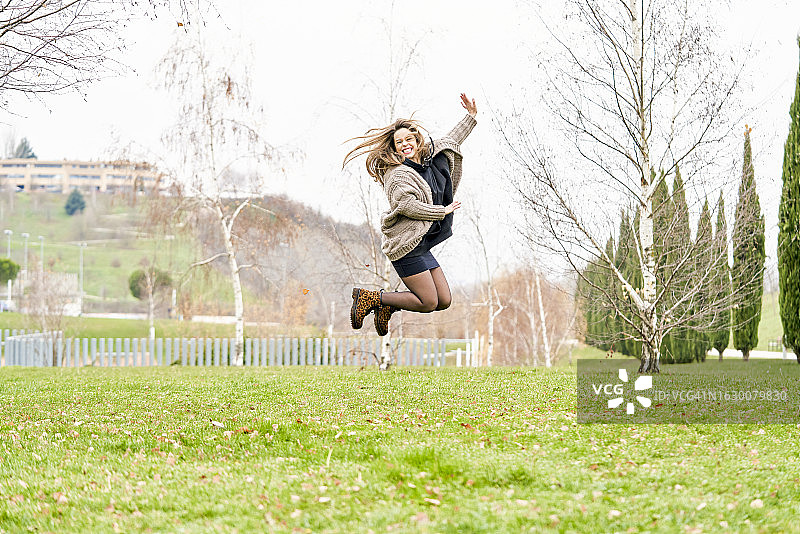 年轻女人在公园跳跃微笑，享受户外时光图片素材
