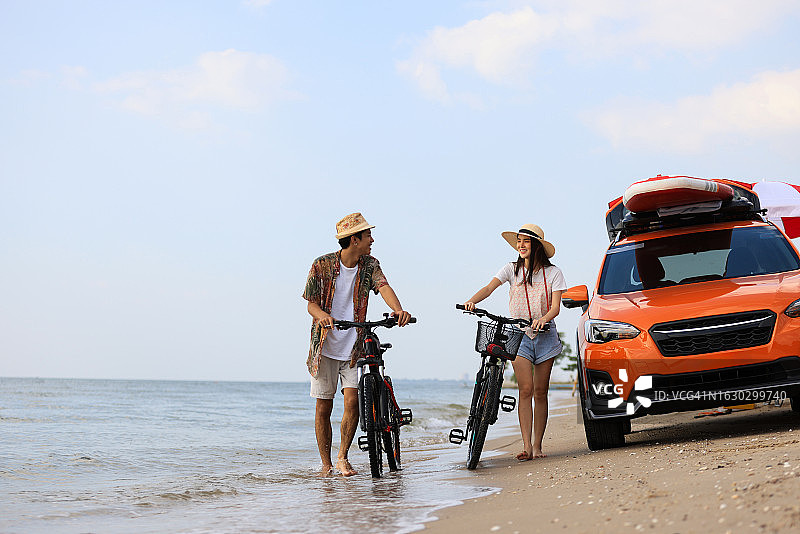 一对年轻夫妇在海滩边，橙色汽车背景图片素材