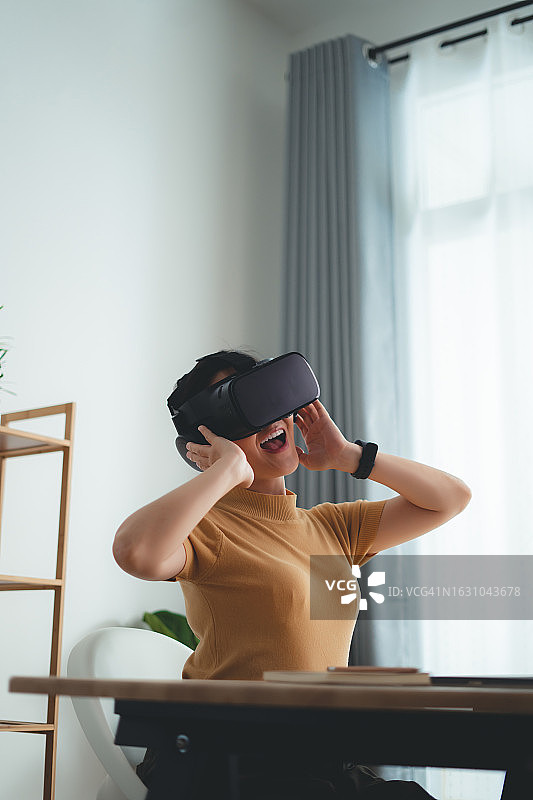 亚洲女性在家庭办公室里戴着VR头显，感到高兴并微笑图片素材