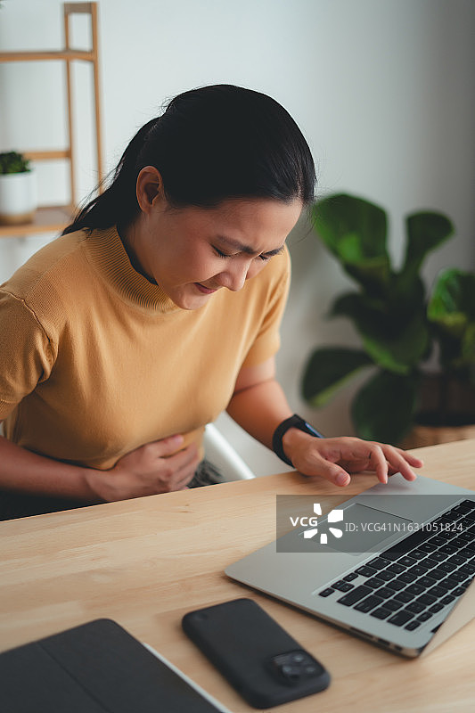 在家居办公室感到胃痛的亚洲女人图片素材