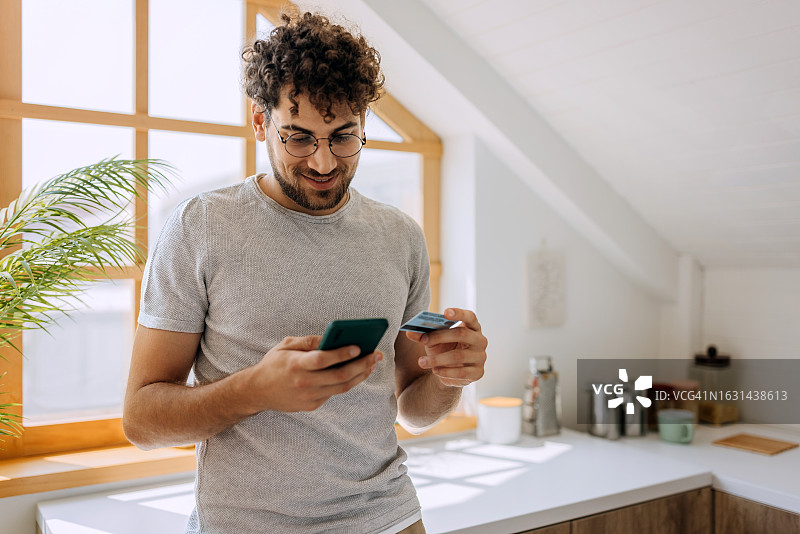 年轻休闲男人在厨房里在线购物图片素材