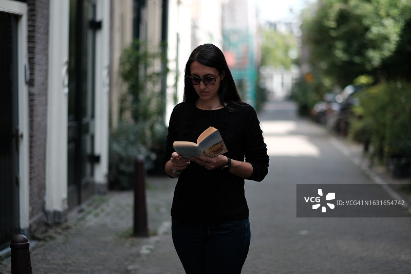 女孩在街上边走边读书图片素材