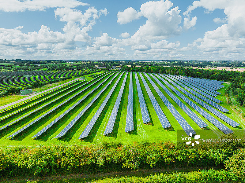 阳光明媚的郊区绿色田野上的太阳能电池板鸟瞰图图片素材