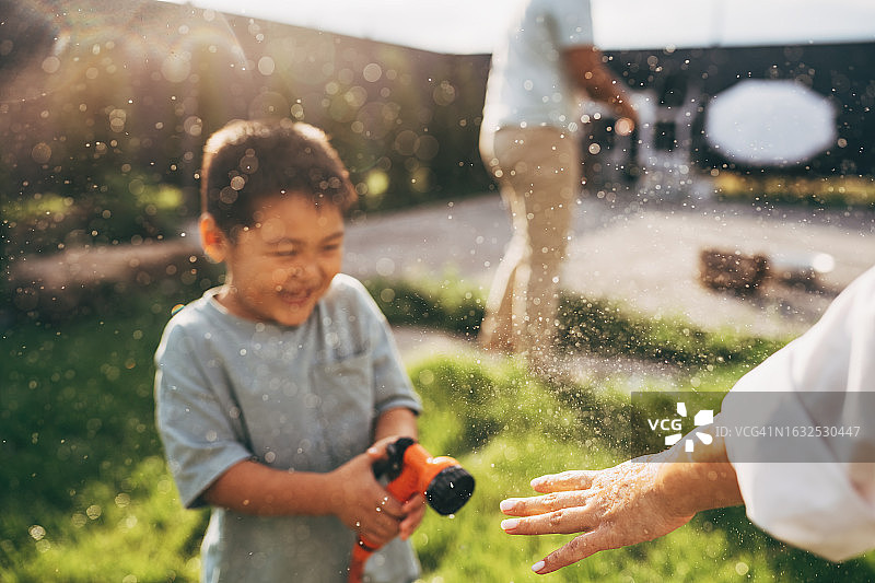 在院子里浇草坪的小亚裔男孩图片素材