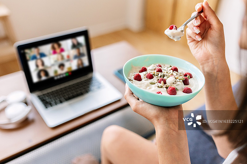 年轻女学生或自由职业者在家中沙发上用笔记本电脑进行视频通话，同时享用早餐图片素材
