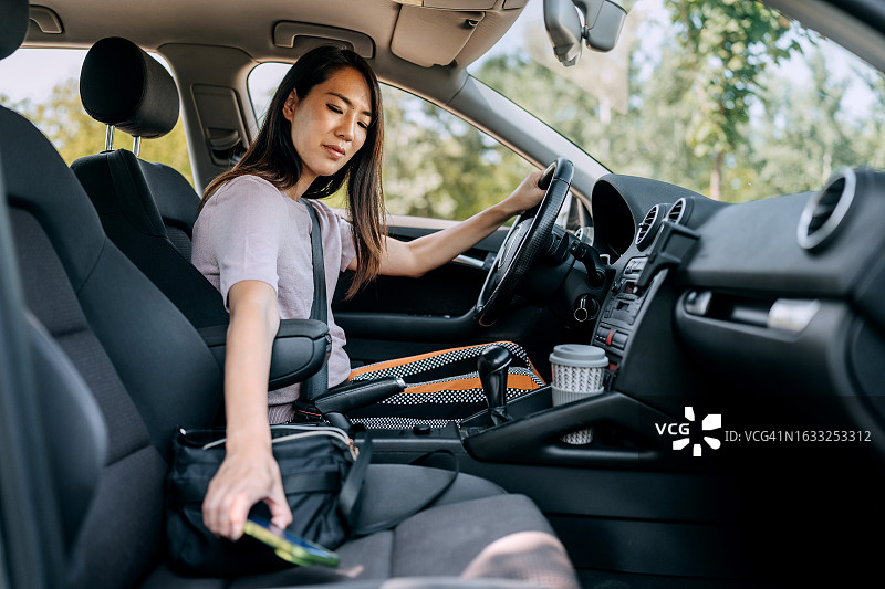 开车时伸手拿手机的女子侧视图图片素材