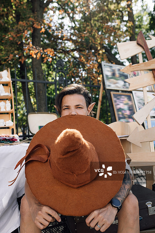 在街头集市工艺品摊位旁休息，手拿手工毡帽的快乐中年女手工艺人图片素材