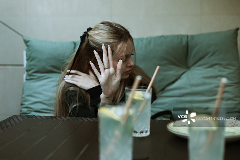 迷人的少女坐在咖啡馆的沙发上，桌子上放着饮料，拒绝拍照图片素材