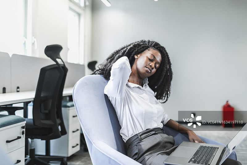 在办公室用笔记本电脑工作，颈椎疼痛的年轻黑人女性图片素材