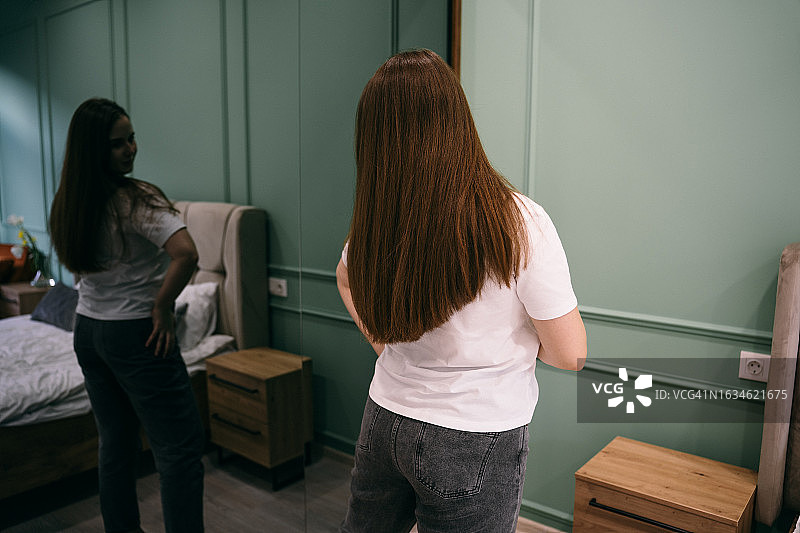 在家看着镜子里自己倒影的年轻女人图片素材