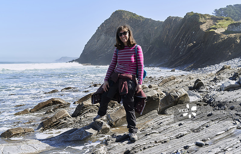 微笑的女人在祖马亚海岸，背着蓝色背包，戴着墨镜图片素材