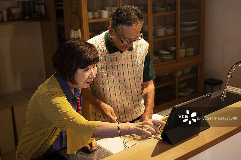 老年夫妇在厨房里一边查阅平板电脑上的食谱，一边享受烹饪的乐趣图片素材