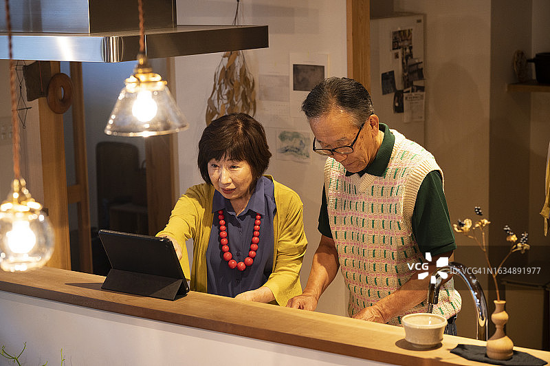 老年夫妇在厨房里一边查阅平板电脑上的食谱，一边享受烹饪的乐趣图片素材