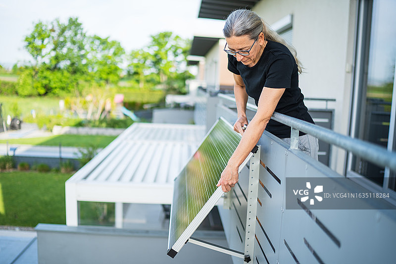 在阳台房屋上调整太阳能电池板的女人图片素材