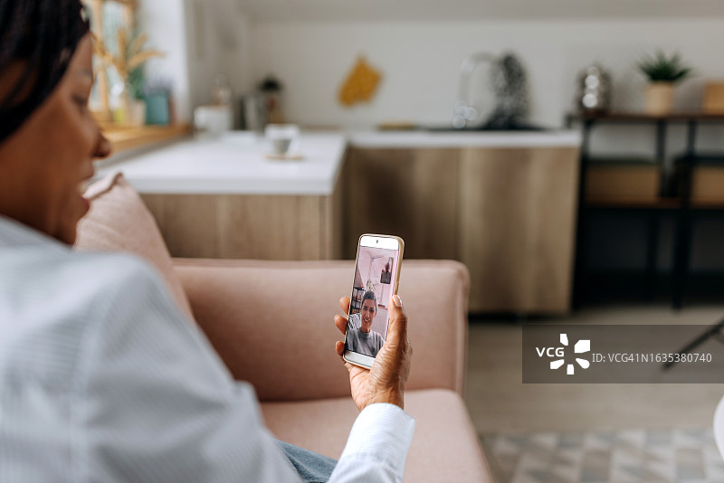 女人在家中沙发上与朋友进行视频通话的肩部视角图片素材