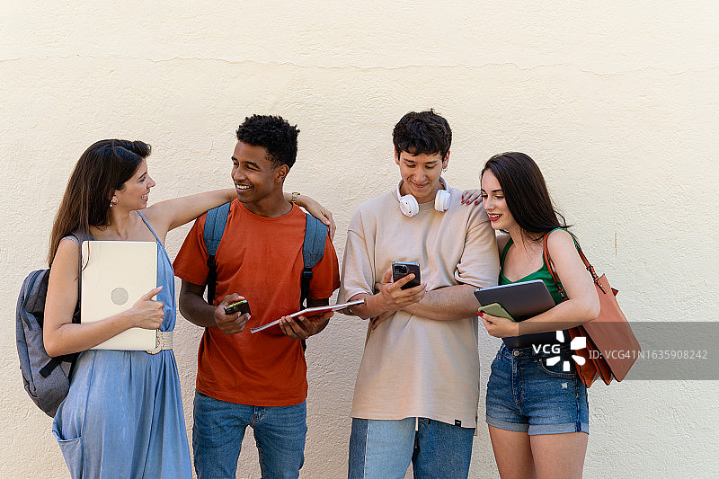 在街上拿着笔记本电脑、平板电脑和笔记本电脑的年轻学生们高兴地笑着图片素材
