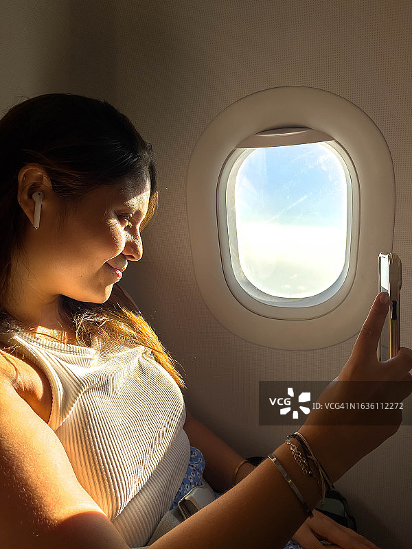 乘坐飞机靠窗座位，戴着耳机自拍的拉丁裔女人图片素材