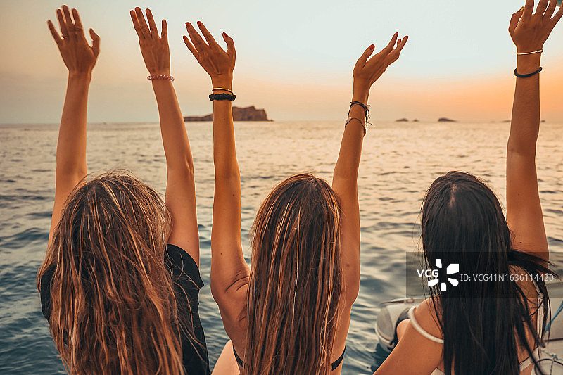 三名女性朋友在伊比萨岛日落时分航行庆祝图片素材