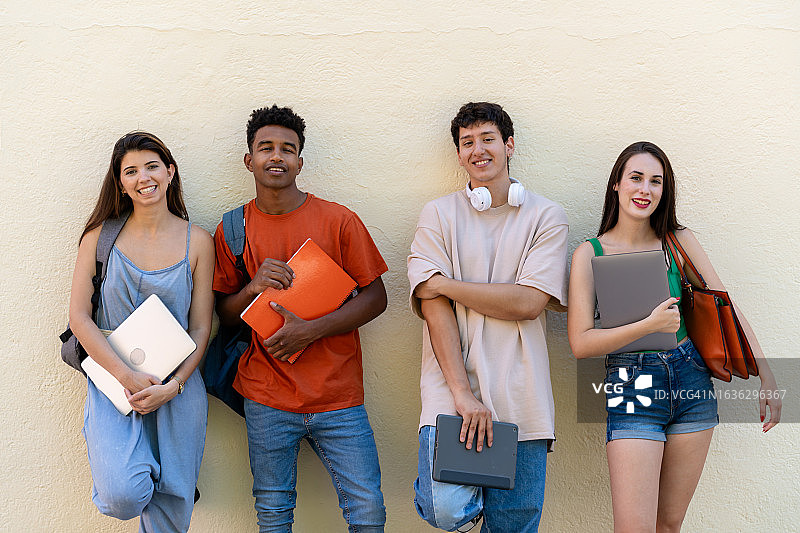 在街上拿着笔记本电脑、平板电脑和笔记本电脑的年轻学生们高兴地笑着图片素材