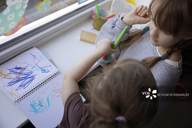 两个孩子在窗台上用毡尖笔在素描簿上绘画的高空景观图片素材