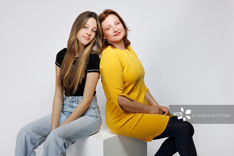 与中年母亲背靠背看着镜头的少女图片素材