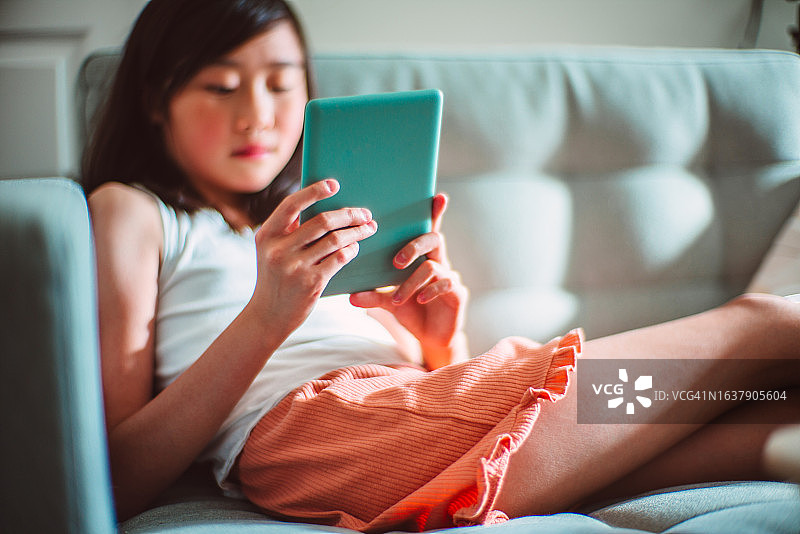 快乐的少女在家用电子阅读器看书图片素材