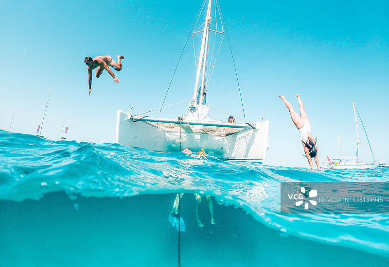 情侣纵身跳入福门特拉岛天堂般海域（乘双体船航行）的半水下视角图片素材