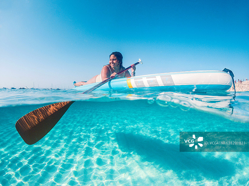 福门特拉岛度假期间，拉丁女人躺在桨板上划船的水下半景图片素材