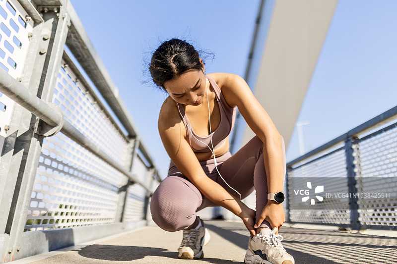 年轻女人在桥上慢跑时腿部受伤图片素材