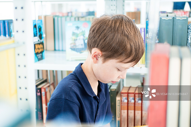 11岁男孩在图书馆书架间阅读图片素材