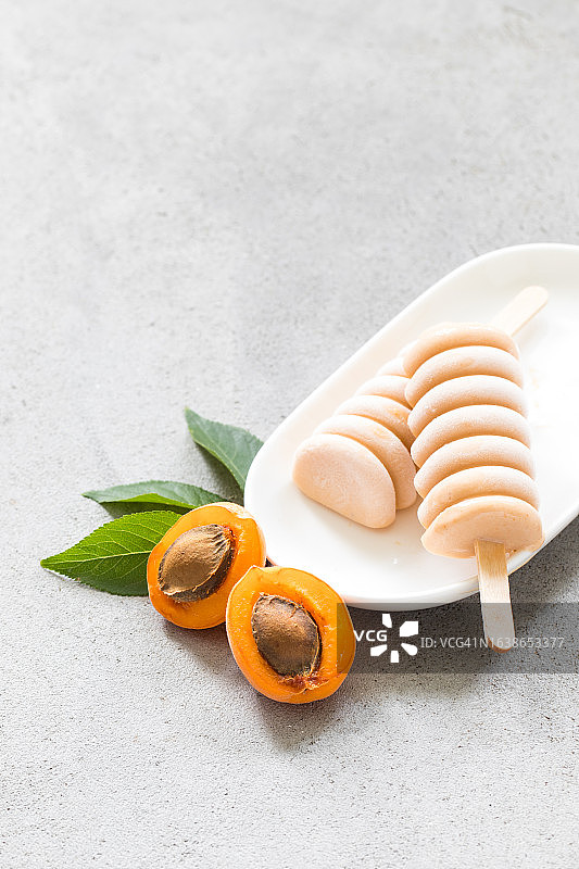 盘中木棍上的杏子冰淇淋，浅灰色背景，特写图片素材